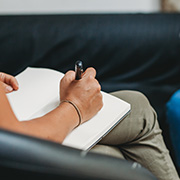 person writing in a notebook seated on a black couch focusing on ideas related to 11 different themes