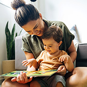 a mother reading a colorful storybook to her young child in a cozy living room surrounded by plants promoting early literacy and bonding time of twelve months old