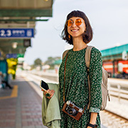 smiling young woman with sunglasses and camera standing at train station wearing green dress and carrying backpack travel lifestyle 4 exploring adventures