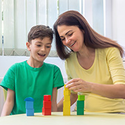 a boy and a woman playing with colorful building blocks while smiling together focused on stacking the blocks in a fun educational activity for children aged 13 and under