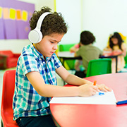 boy in headphones drawing at table in classroom environment with other children engaged in creative activities promoting focus and imagination for students ages nine