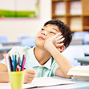 young boy daydreaming in a classroom surrounded by stationery with a focus on learning and imagination for 7 year olds