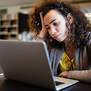 woman with curly hair looking stressed at laptop in a study environment trying to solve a problem possibly related to 7 challenges